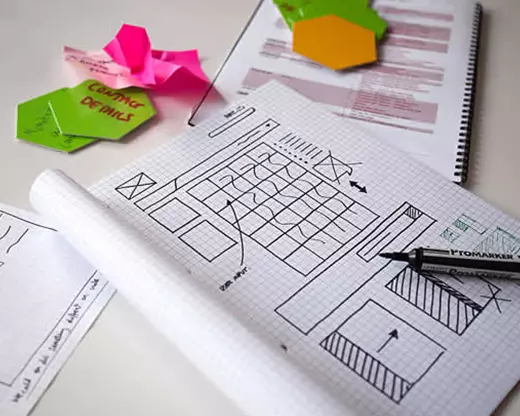 A sketch of a layout on graph paper with sticky notes, colored hexagon cutouts, and a pen placed on top.