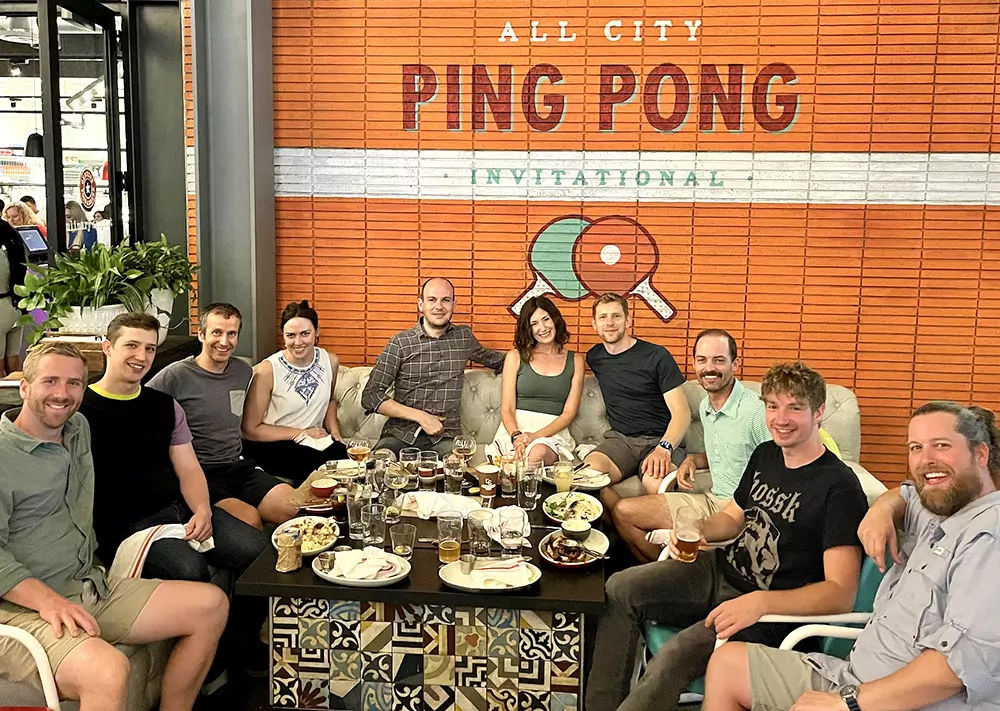 A man holding a microphone and presenting in front of a red screen with his website and Twitter handle displayed.